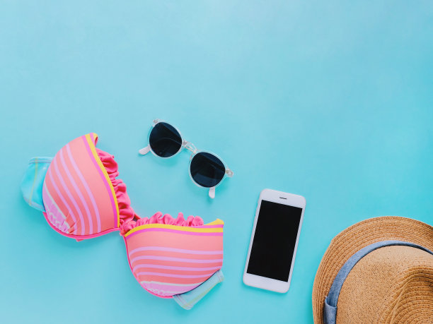 平铺的夏季用品与色彩缤纷的比基尼，太阳镜，帽子和智能手机在绿色背景，拷贝空间图片下载