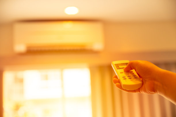 在炎热的夏天，用遥控器手动调节空调温度到壁挂式空调家庭冷却系统图片下载