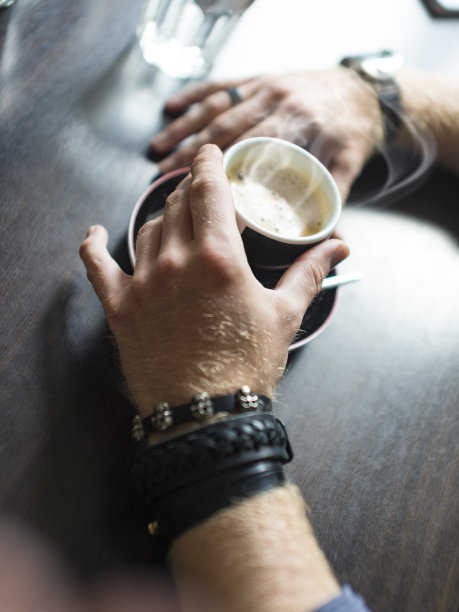 潮人的手拿着一杯咖啡在咖啡馆的桌子上，特写图片下载