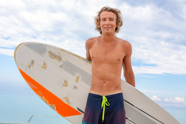 英俊的男子走在白色的空白冲浪板等待海浪冲浪点在海洋海岸。运动、健身、自由、快乐、新现代生活、潮人的理念。图片下载