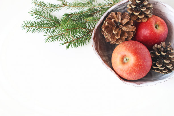 红色的苹果和松果在陶瓷碗和云杉树枝在白色桌子的背景特写。圣诞假期风格的股票照片。冬天的食物成分。平躺，俯视图。图片下载