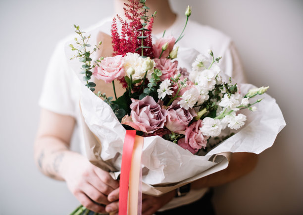 非常好的年轻人拿着美丽的鲜花盛开的玫瑰，菊芋，桉树在白色和紫色的颜色在灰色的背景图片下载