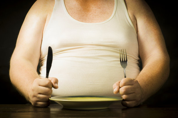 一个手里拿着刀叉的胖子坐在盘子上面图片下载