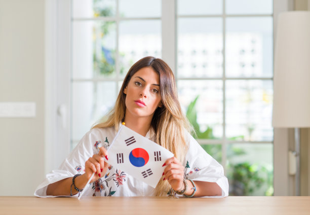年轻女子在家中举着韩国国旗，聪明的脸上带着自信的表情认真思考图片下载