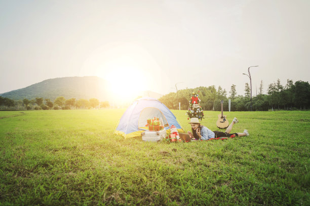 在秋天的黄昏，一个年轻的亚洲女子在草地上用手机摆拍自己的照片，在一个日落的圣诞户外派对上。图片下载