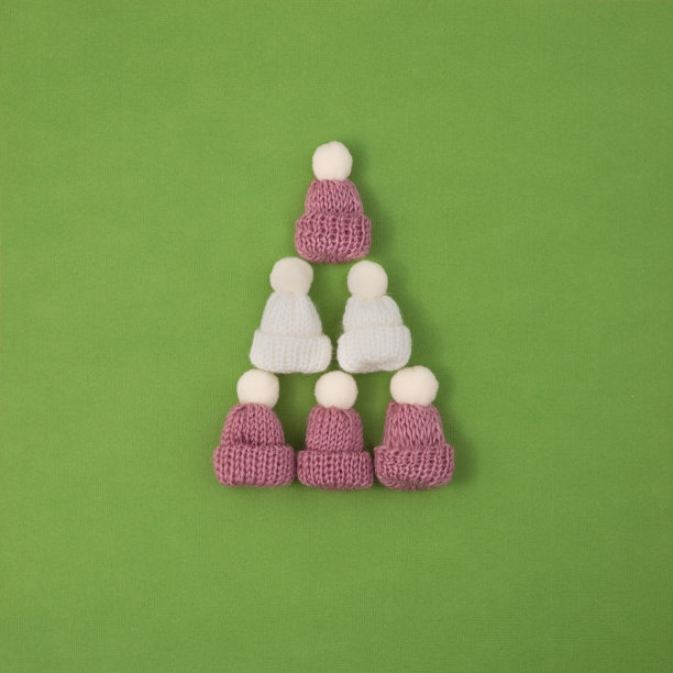 这棵圣诞树由绿色背景上的彩色针织帽和绒球组成。图片下载