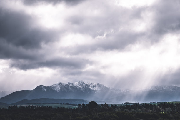 令人惊叹的景色，在一个多云的日子里，阳光透过云越过雪山。戏剧性的照片风格。图片下载