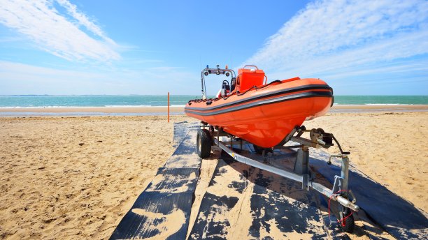 在一个阳光明媚的日子里，红色巡逻艇装载在一辆拖车上停靠在海滩上图片下载
