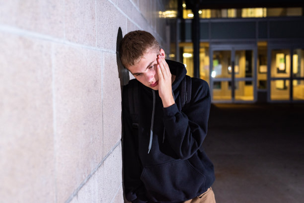 晚上，一个沮丧的少年倚靠在一所高中的砖墙上。图片下载