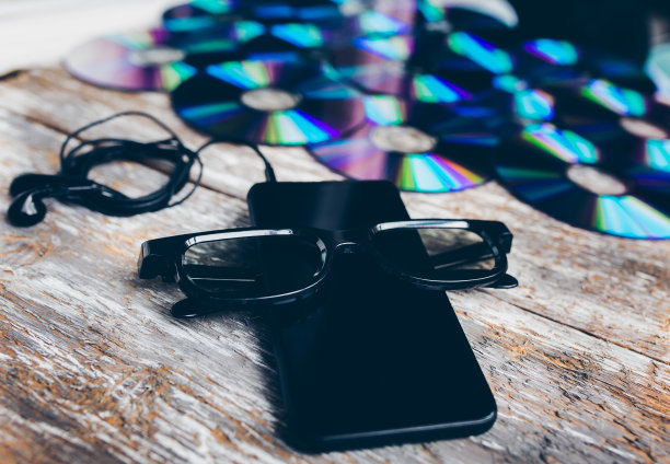 许多Cd光盘躺在古老的木头桌子上。全息颜色。黑色的智能手机、眼镜和耳机就在附近。音乐和现代科技照片。数字的动机。图片下载