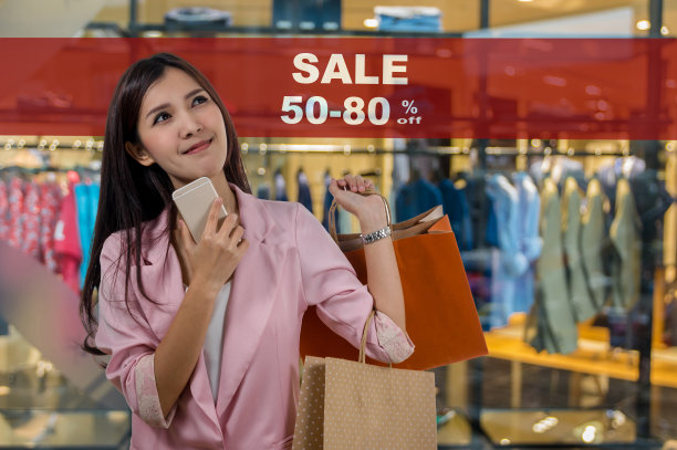 快乐年轻的亚洲女人购物在快乐的感觉和拿着产品纸袋在销售50-80%的模拟广告展示框架设置在抽象模糊照片的服装店图片下载