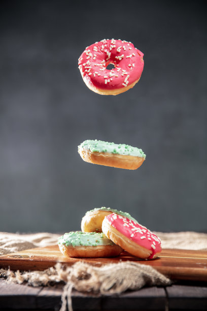 质朴的餐桌上点缀着粉色和绿色糖霜的甜甜圈。照片的垂直方向。图片下载