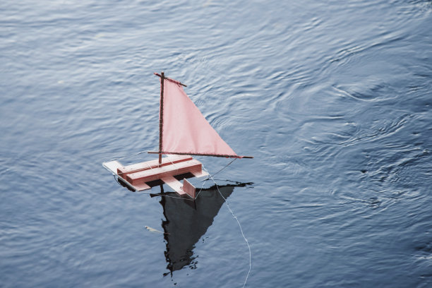 粉红色帆的玩具船在夕阳的照耀下漂浮在水面上。图片下载