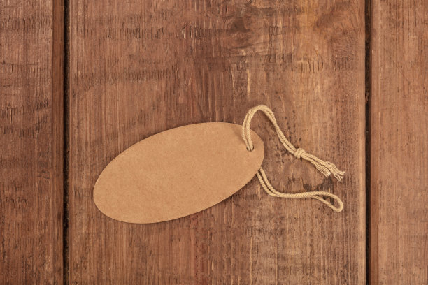 一张椭圆形棕色牛皮纸标签或价格标签的照片，从顶部拍摄，背景是黑色的乡村木，并有文字的地方图片下载