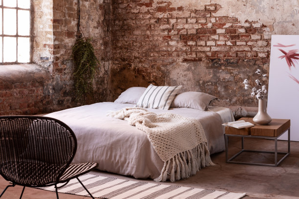 床上的毯子和枕头在现代卧室的室内，桌子和椅子上有花。真实的照片图片下载