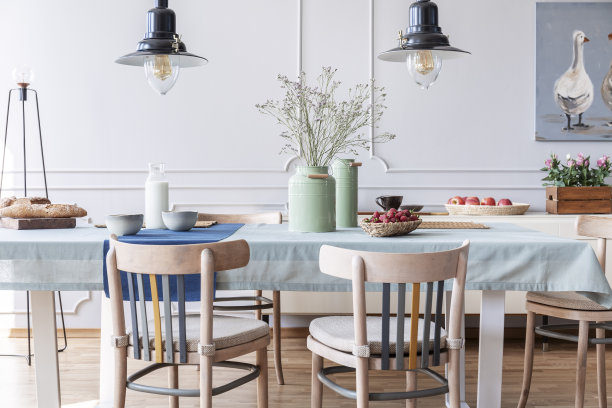 在白色的小木屋餐厅里，餐桌旁的木椅上摆放着鲜花和食物，室内配有灯具和海报。真实的照片图片下载