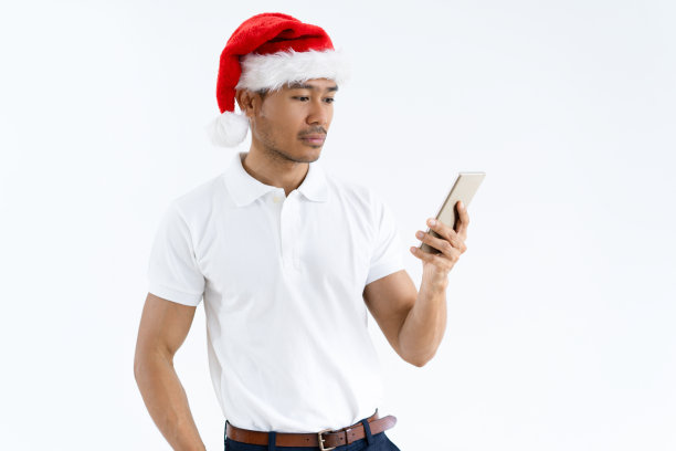 严肃的亚洲男人戴着圣诞老人帽，使用智能手机图片下载