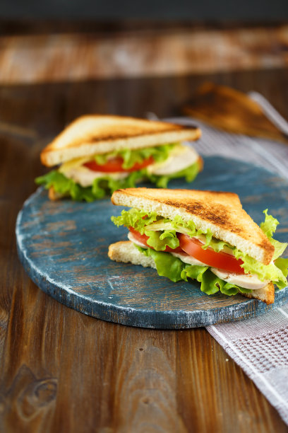两个美味的三明治与鸡肉，西红柿，生菜，奶酪在木盘子上，在黑暗的背景图片下载