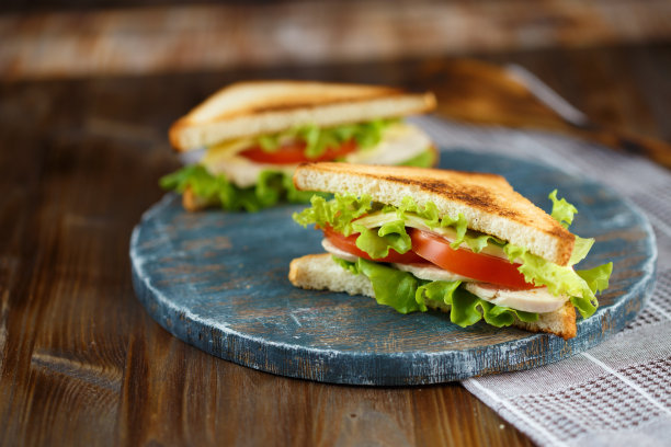 两个美味的三明治与鸡肉，西红柿，生菜，奶酪在木盘子上，在黑暗的背景图片下载