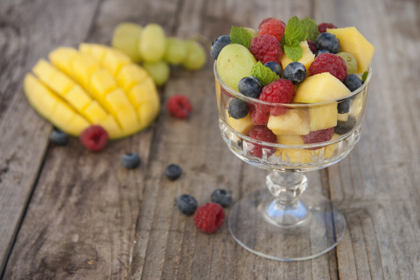 美味的水果沙拉玻璃-覆盆子，芒果，蓝莓，葡萄，薄荷叶。木桌，质朴的背景。图片下载