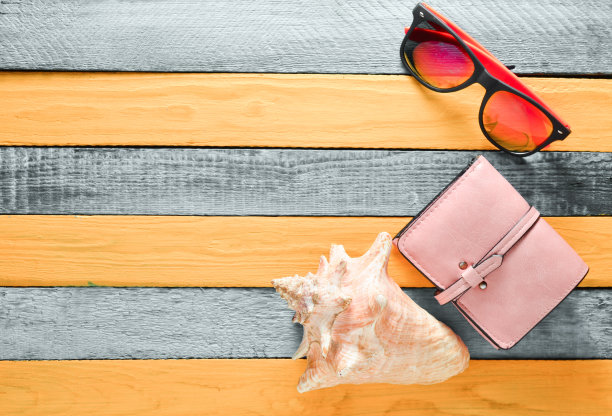 女性海滩配件在一个蓝色的黄色木制背景。旅行的概念。壳,眼镜,钱包。平的。副本的空间。图片下载