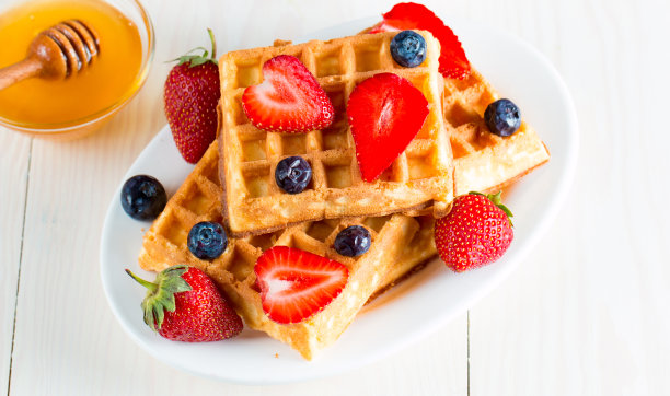 新鲜的自制食物的照片，浆果比利时华夫饼与蜂蜜，巧克力，草莓，蓝莓，枫糖浆和奶油。健康的早餐甜点搭配果汁。图片下载