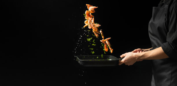 专业厨师用蔬菜烹制虾。烹饪海鲜，健康的素食，和食物在一个黑暗的背景。水平的观点。图片下载