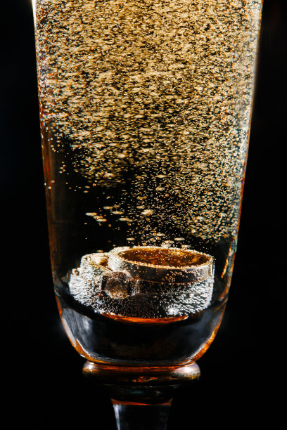 结婚戒指放在有金色泡泡的香槟酒杯里。近景黑色背景图片下载