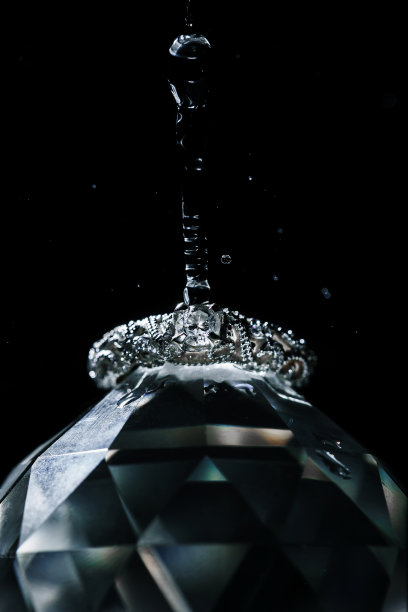 白色的结婚戒指躺在大钻石上，水滴从上面落下。垂直拍摄与黑暗的黑色背景图片下载