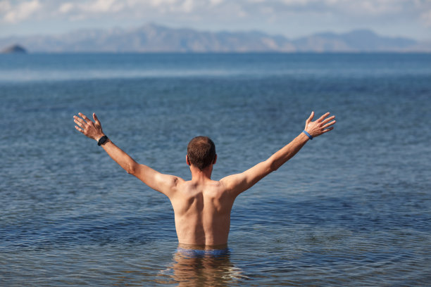 一个年轻人在大海里张开双臂，背对着群山图片下载