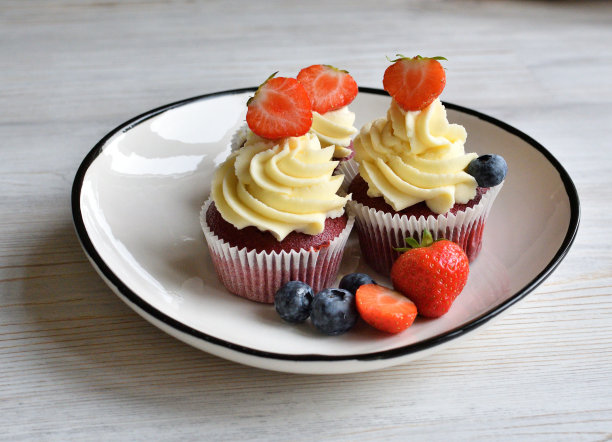 在白色的木质表面上放着浆果的美味纸杯蛋糕。红色天鹅绒蛋糕。图片下载