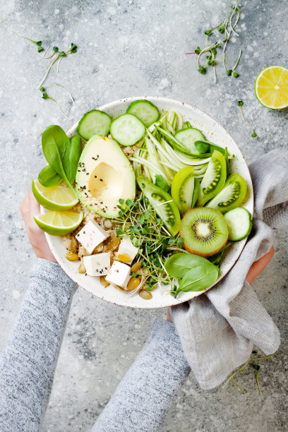 女孩拿着素食排毒佛碗，里面有奎奴亚藜，鳄梨，西葫芦面条，黄瓜，番茄，酸橙，猕猴桃，豆腐，菠菜，微绿色蔬菜，披萨。图片下载