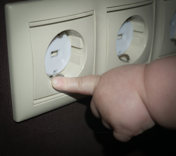 婴儿的手伸向覆盖着安全插头的电源插座。婴儿和儿童安全概念图片下载