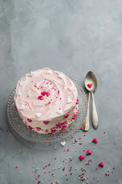 蛋糕有小心形和彩色的点缀与两个勺子在灰色的背景。浪漫爱情的背景。情人节卡片。圣瓦伦丁，母亲节，生日蛋糕背景与空间的文本。垂直的。图片下载