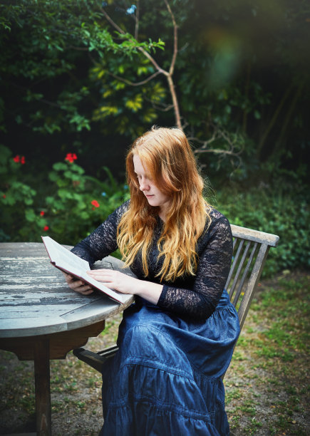 漂亮的女孩长着红色的头发在户外看书图片下载