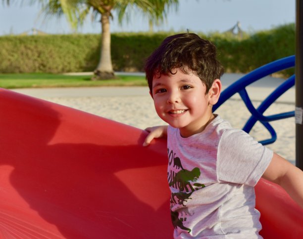 坐在红色滑梯上的微笑男孩图片下载