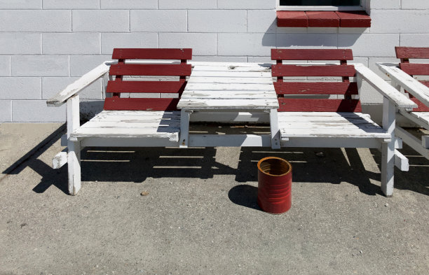栗色和白色的室外木制夏日长椅，映衬着白色砖混砌块墙的背景，红色的水桶作为烟灰缸。吸烟区和吸烟区概念图片下载