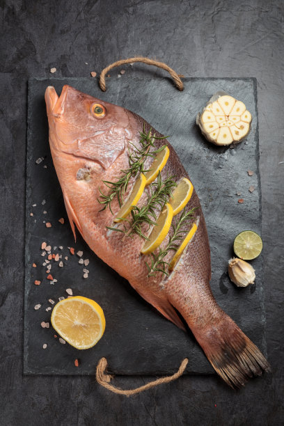 新鲜腌制的红鲷鱼配上柠檬片，大蒜和迷迭香香草，深色背景，俯视图。垂直组成图片下载