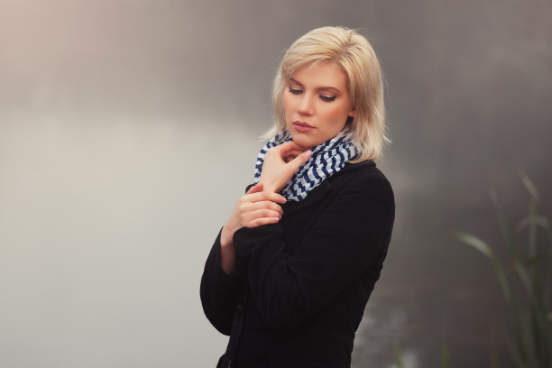 穿着黑色大衣的悲伤年轻时尚的女人在雾中走在湖边图片下载