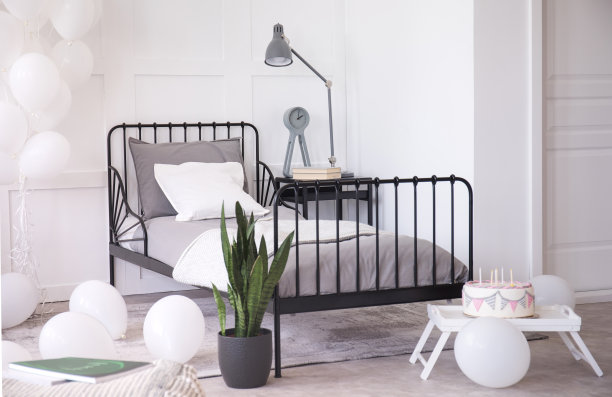 生日蛋糕与蜡烛，绿色植物在黑色花盆和白色气球在明亮优雅的卧室内部，真实的照片图片下载