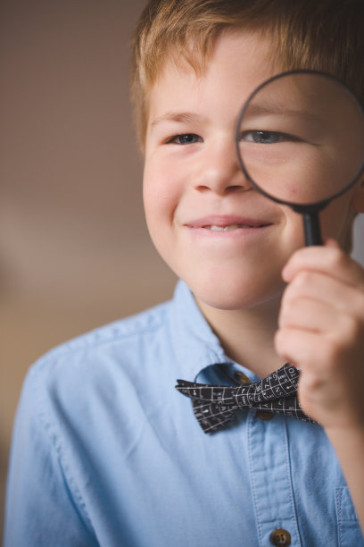 一个穿蓝色衬衫的可爱的小男孩通过放大镜看的照片。透过放大镜观看的孩子。在室内。教育与学习理念。图片下载