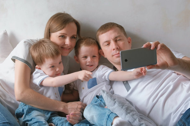 爸爸用手机拍家庭自拍。妈妈，爸爸和两个双胞胎弟弟正在学步。图片下载