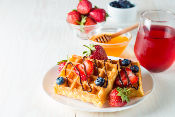 新鲜的自制食物的照片，浆果比利时华夫饼与蜂蜜，巧克力，草莓，蓝莓，枫糖浆和奶油。健康的早餐甜点搭配果汁。图片下载