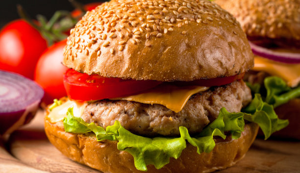 自制汉堡的特写照片，啤酒由牛肉、洋葱、番茄、生菜、奶酪和香料制成。新鲜的汉堡特写在木制的乡村桌子和土豆薯条和薯条。图片下载
