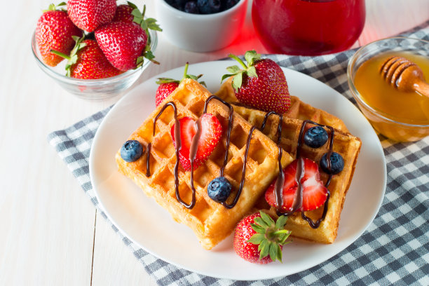 新鲜的自制食物的照片，浆果比利时华夫饼与蜂蜜，巧克力，草莓，蓝莓，枫糖浆和奶油。健康的早餐甜点搭配果汁。图片下载
