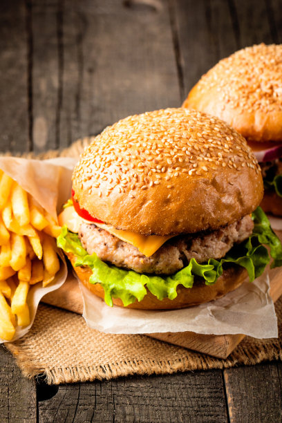 自制汉堡的特写照片，啤酒由牛肉、洋葱、番茄、生菜、奶酪和香料制成。新鲜的汉堡特写在木制的乡村桌子和土豆薯条和薯条。图片下载