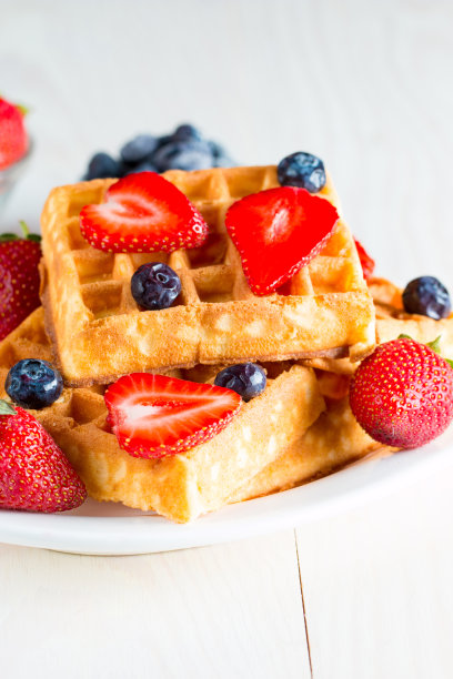 新鲜的自制食物的照片，浆果比利时华夫饼与蜂蜜，巧克力，草莓，蓝莓，枫糖浆和奶油。健康的早餐甜点搭配果汁。图片下载