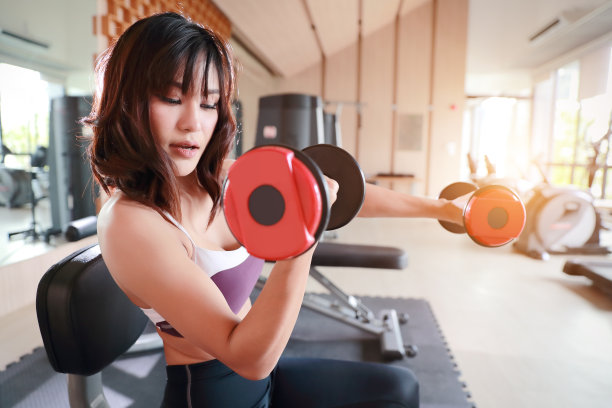 健身女孩举着哑铃在健身房锻炼图片下载