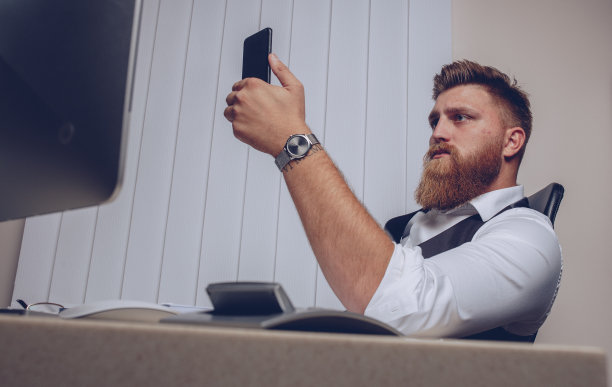 男人们在办公室里查看智能手机，坐在办公桌前摆弄电脑图片下载