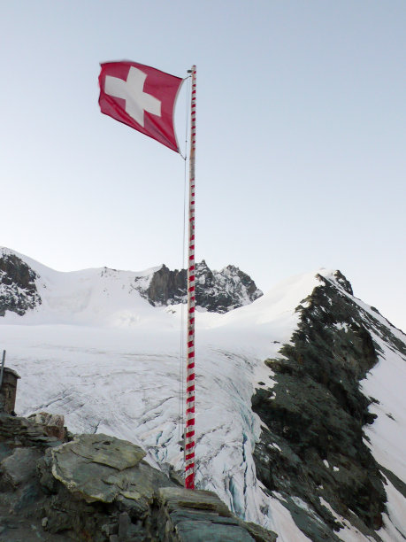 经典的瑞士山地景观，雪山覆盖，瑞士国旗在风中飘扬图片下载